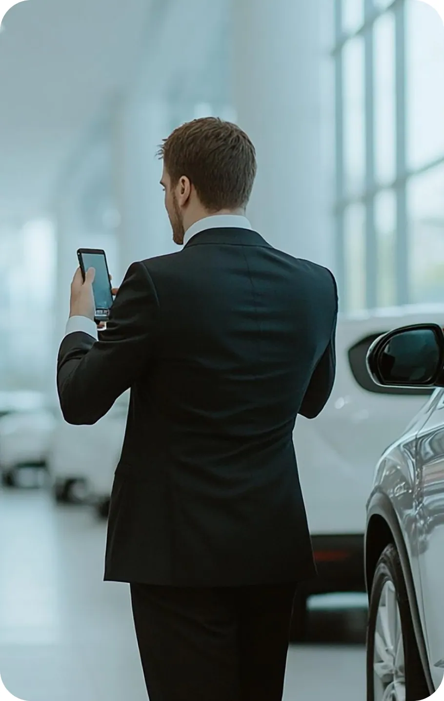 A salesperson standing beside a vehicle, checking a phone