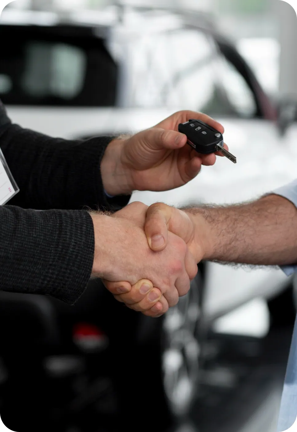 A salesperson handing car keys to a customer with a handshake